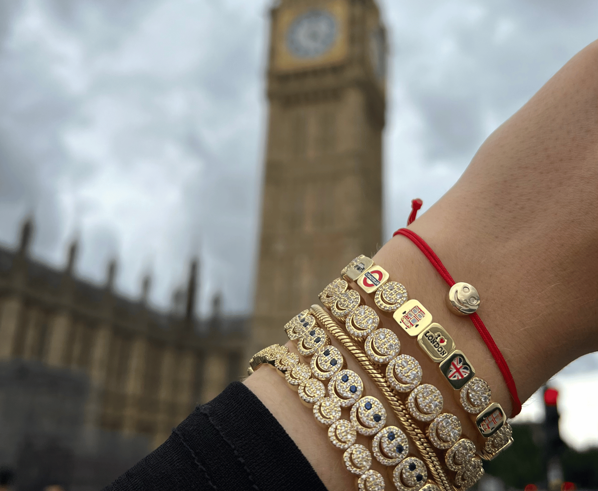 Gold bangles with British flag design on a wrist, blurred background of Big Ben.