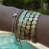 Wrist wearing multiple bracelets with various charms against a blurred natural background