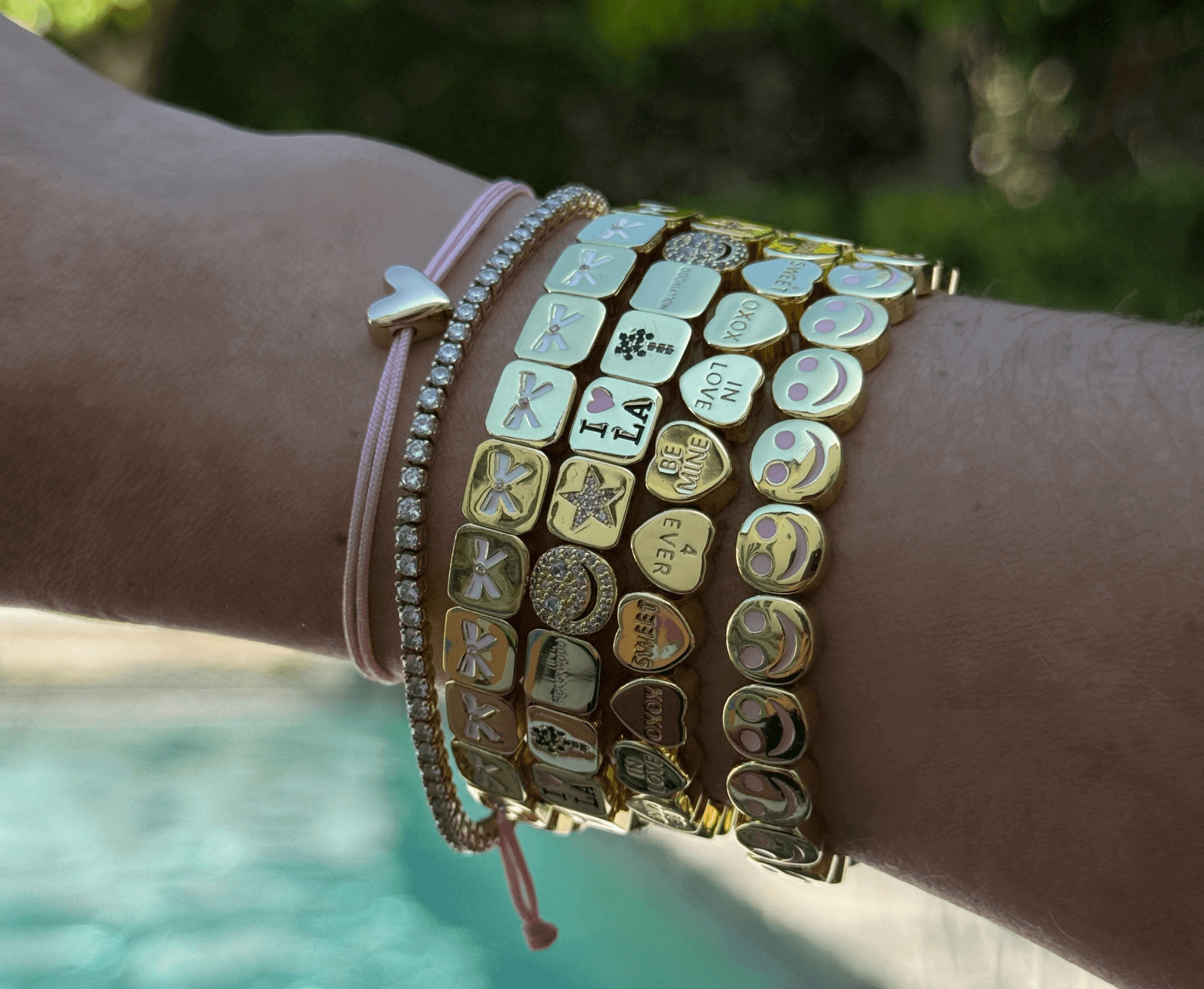 Wrist wearing multiple bracelets with various charms against a blurred natural background