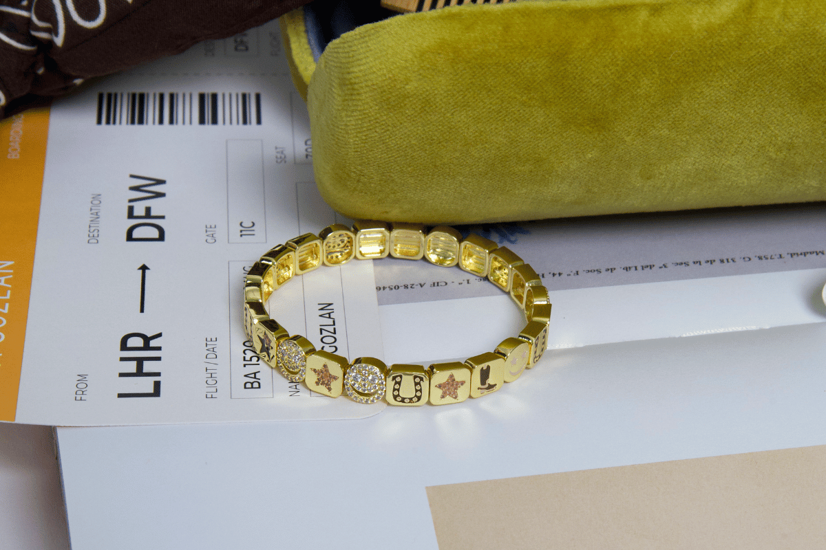 Gold bracelet on top of a flight ticket with a green case in the background