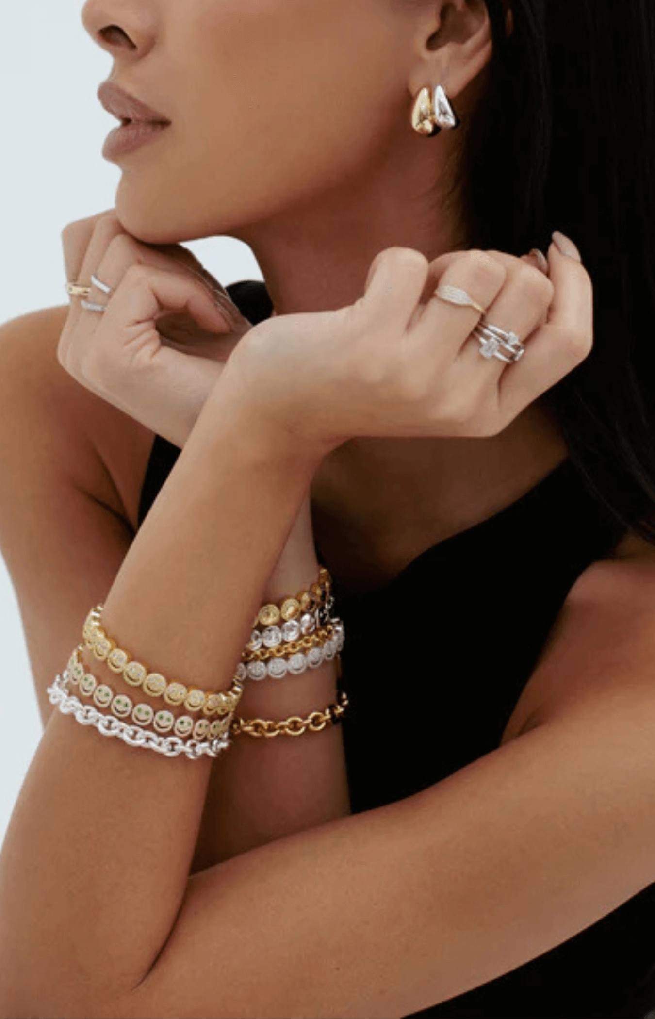 Close-up of a woman's hand wearing multiple gold and silver rings and bracelets against a neutral background.