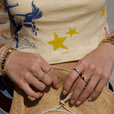Close-up of hands with rings on a woven bag, wearing gold bracelets and a patterned garment.